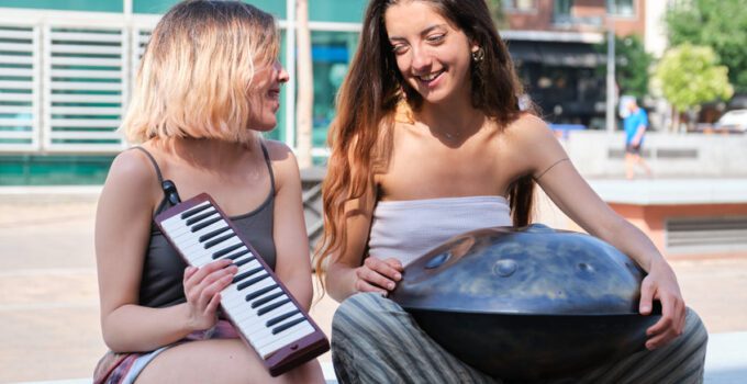 Two women talking and laughing while playing handpand and melodica blow organ.