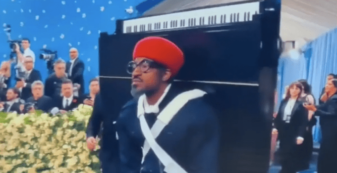 Andre 3000 wearing a baby grand piano to advertise his latest album 7 Piano Sketches